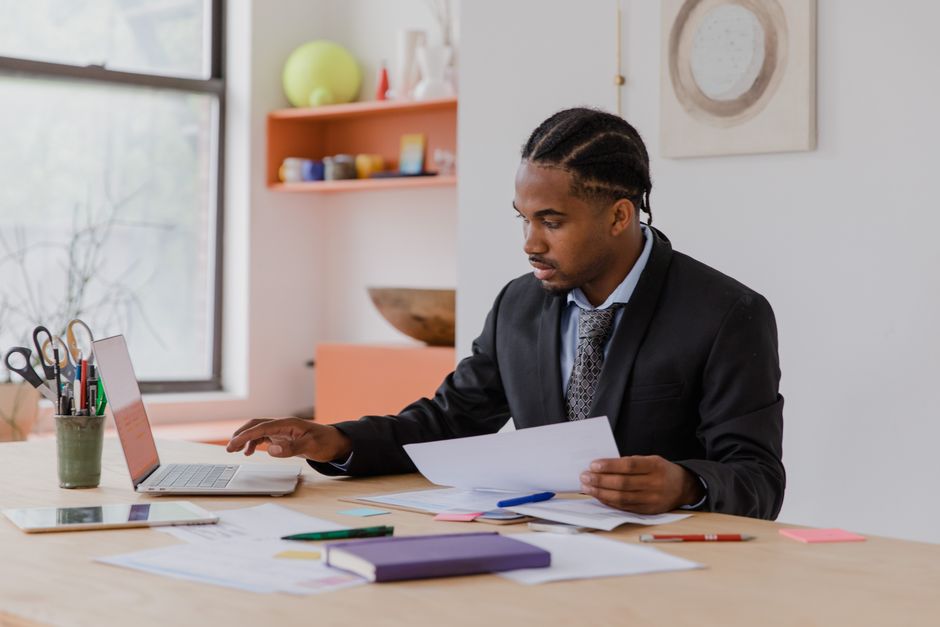Dirigeant d’entreprise comparant des documents comptables sur son bureau avec un ordinateur portable