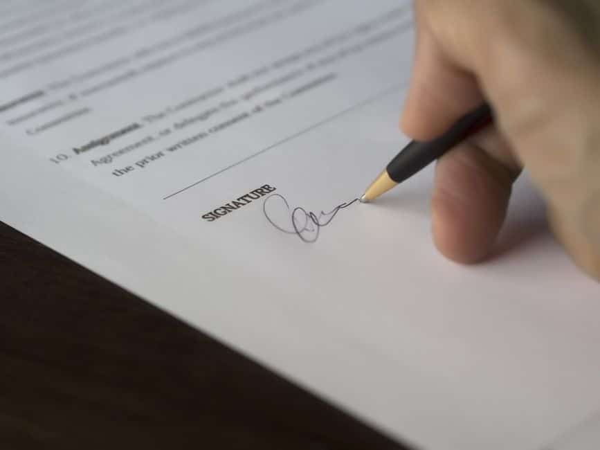 Main signant un contrat au stylo sur un bureau en bois